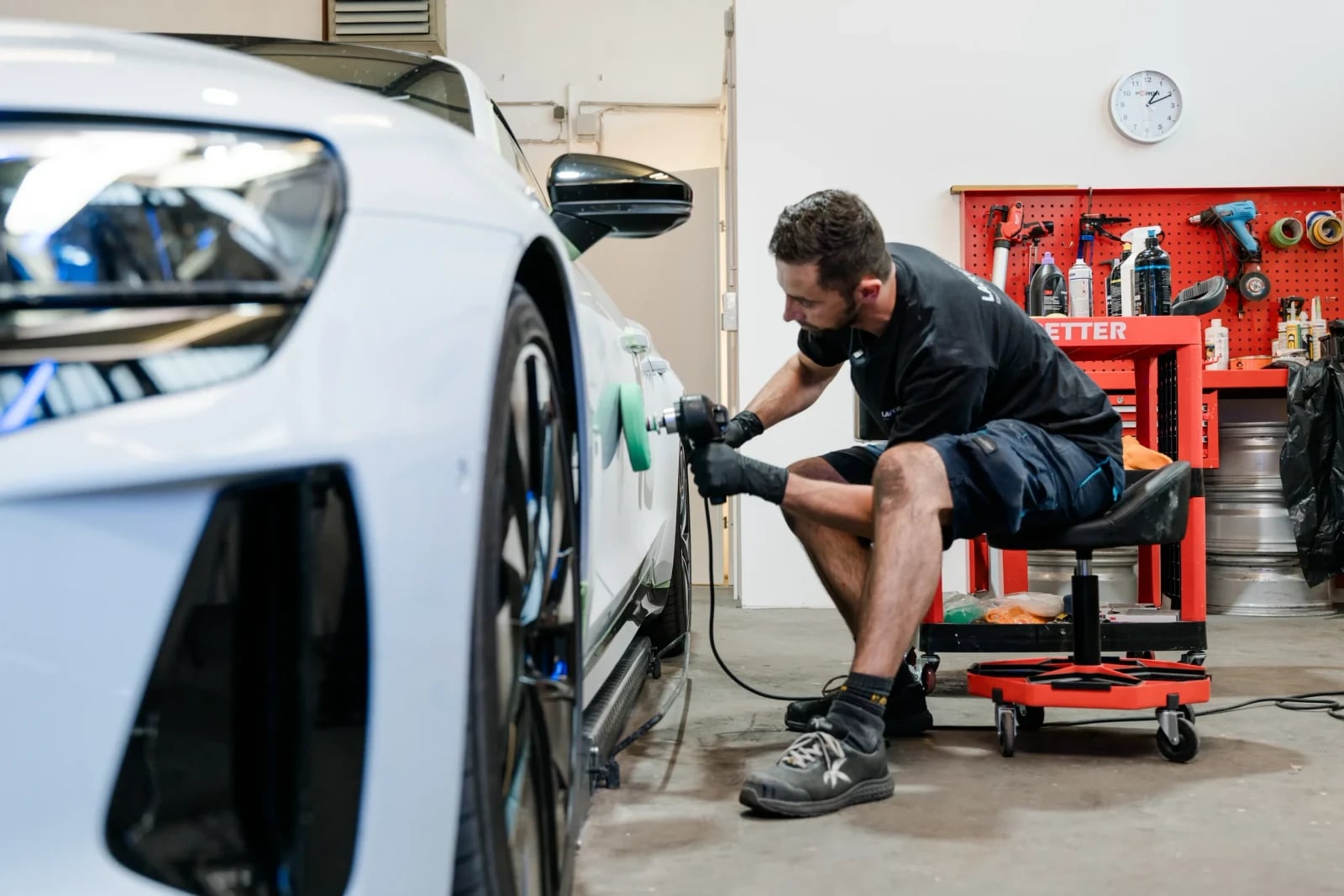 Techniker poliert die Seitenlinie eines weißen Fahrzeugs mit der Poliermaschine in der Werkstatt.