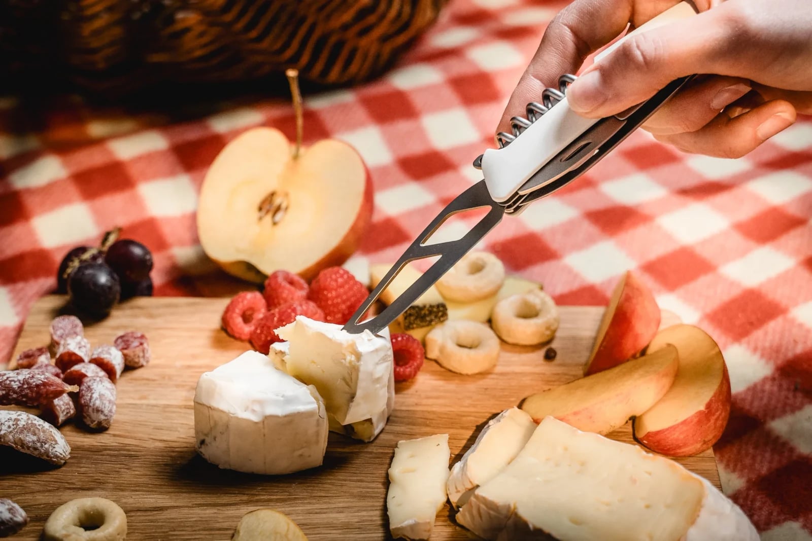 Hand sticht mit der Käsegabel des SWIZA Taschenmessers in ein Stück Weichkäse beim Picknick.