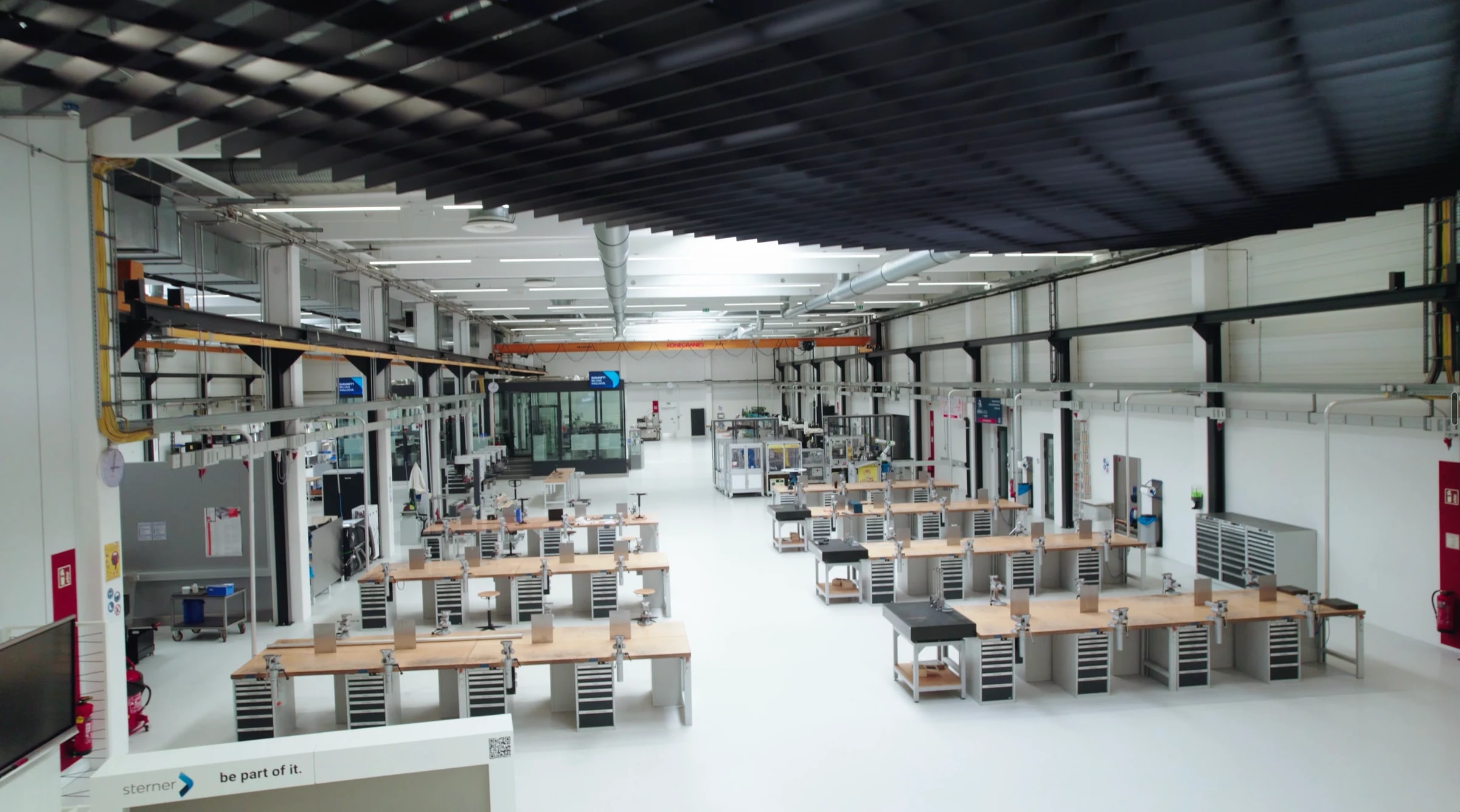Blick von oben in die helle Werkshalle des sterner training center mit Reihen von Werkbänken samt Schraubstöcken und Maschinen im Hintergrund; vorne ein Schriftzug mit „sterner – be part of it.“