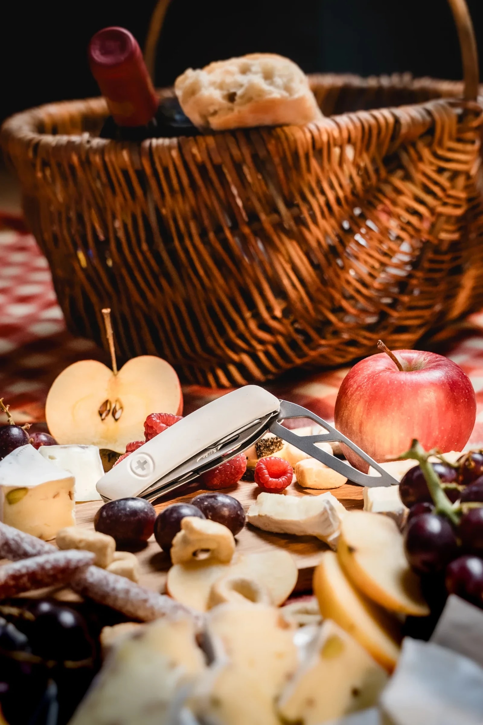 SWIZA Taschenmesser mit ausgeklappter Käsegabel vor einem Weidenkorb mit Wein und Brot.