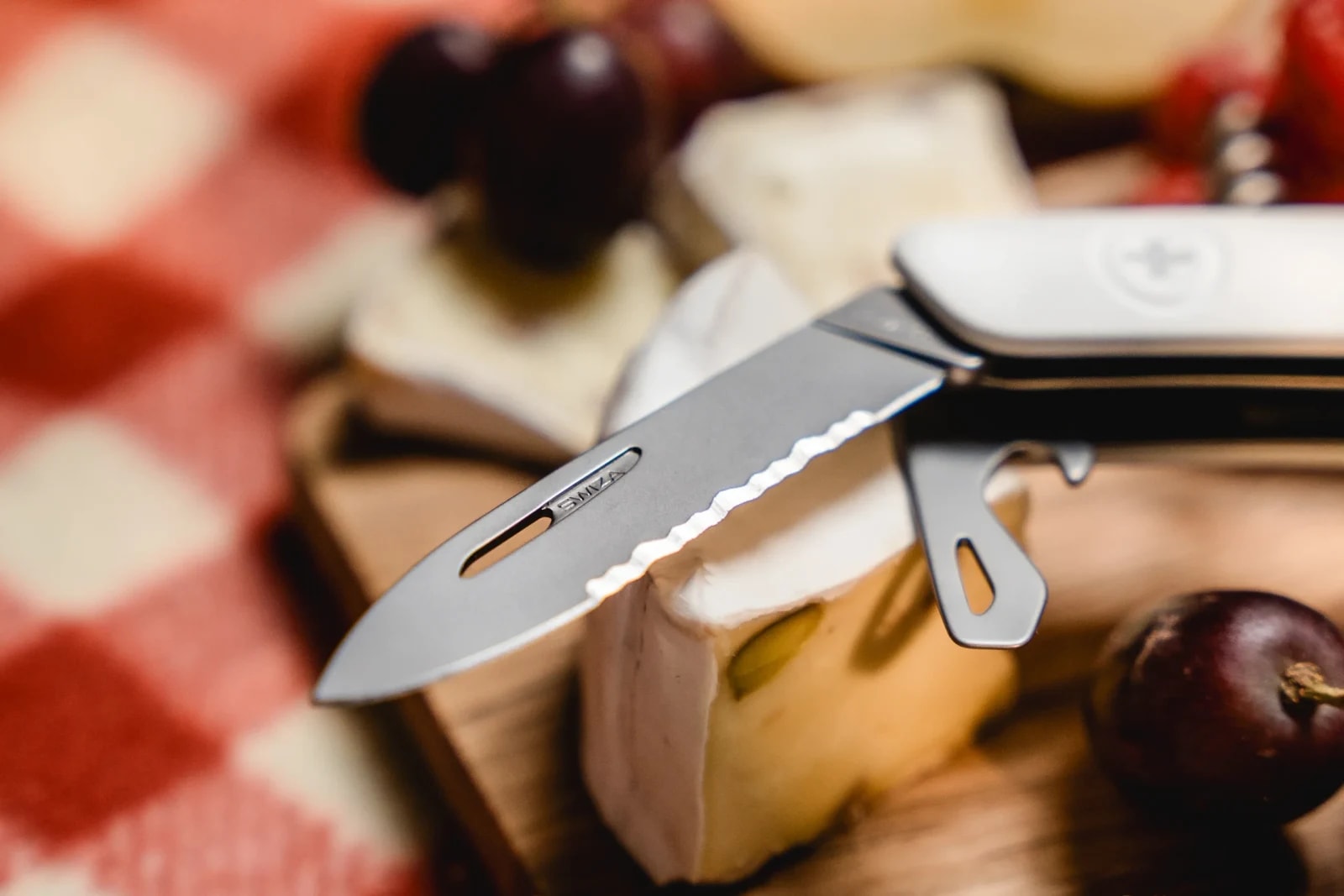 Detail: ausgeklappte Klinge und Werkzeuge des SWIZA Taschenmessers über einem Stück Camembert.