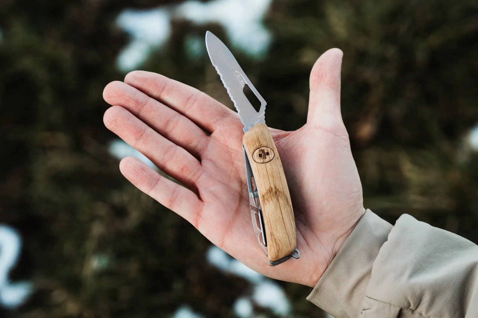 Geöffnetes SWIZA Taschenmesser mit Holzgriff liegt auf einer offenen Handfläche vor Nadelwald.