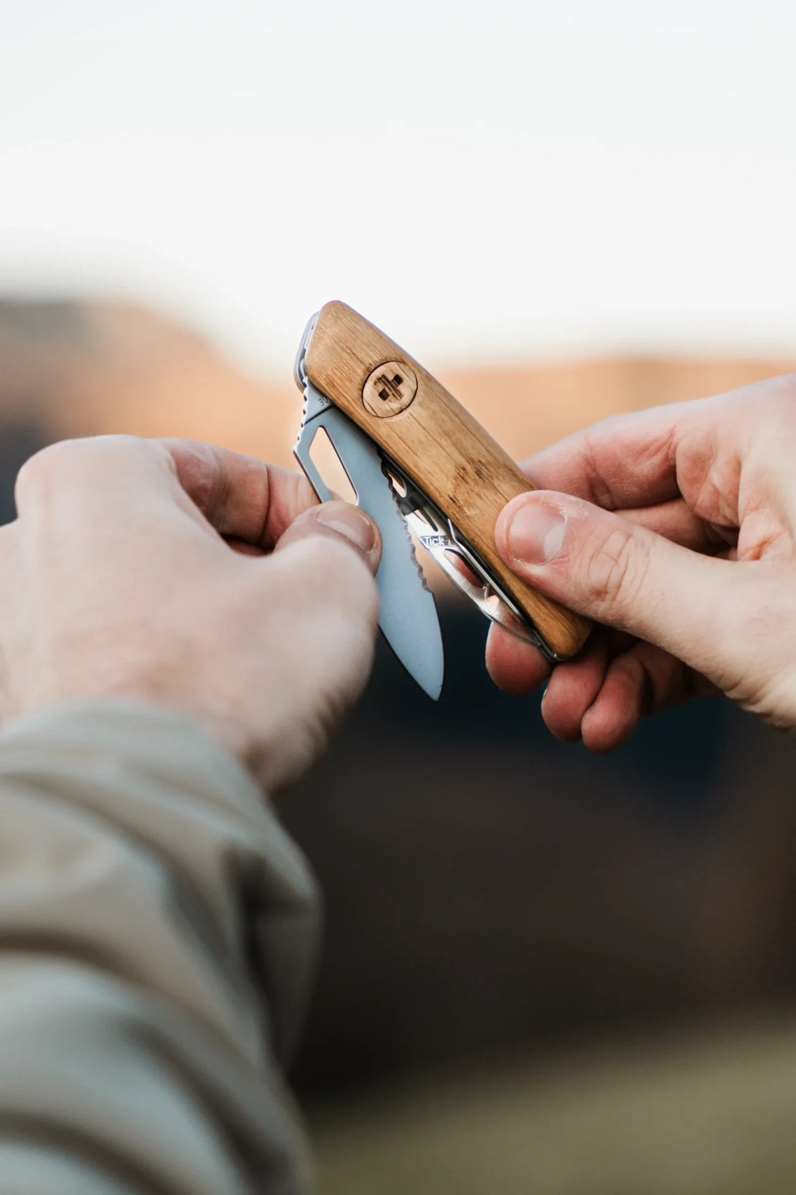 Hände öffnen ein SWIZA Schweizer Taschenmesser mit Holzgriff im Abendlicht.