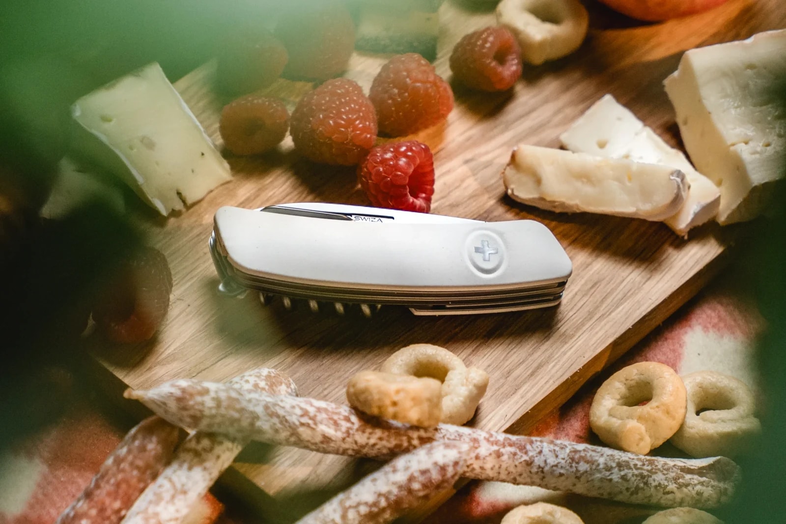 SWIZA Taschenmesser mit weißem Griff auf einem Käsebrett mit Weichkäse, Beeren und Salamisticks.