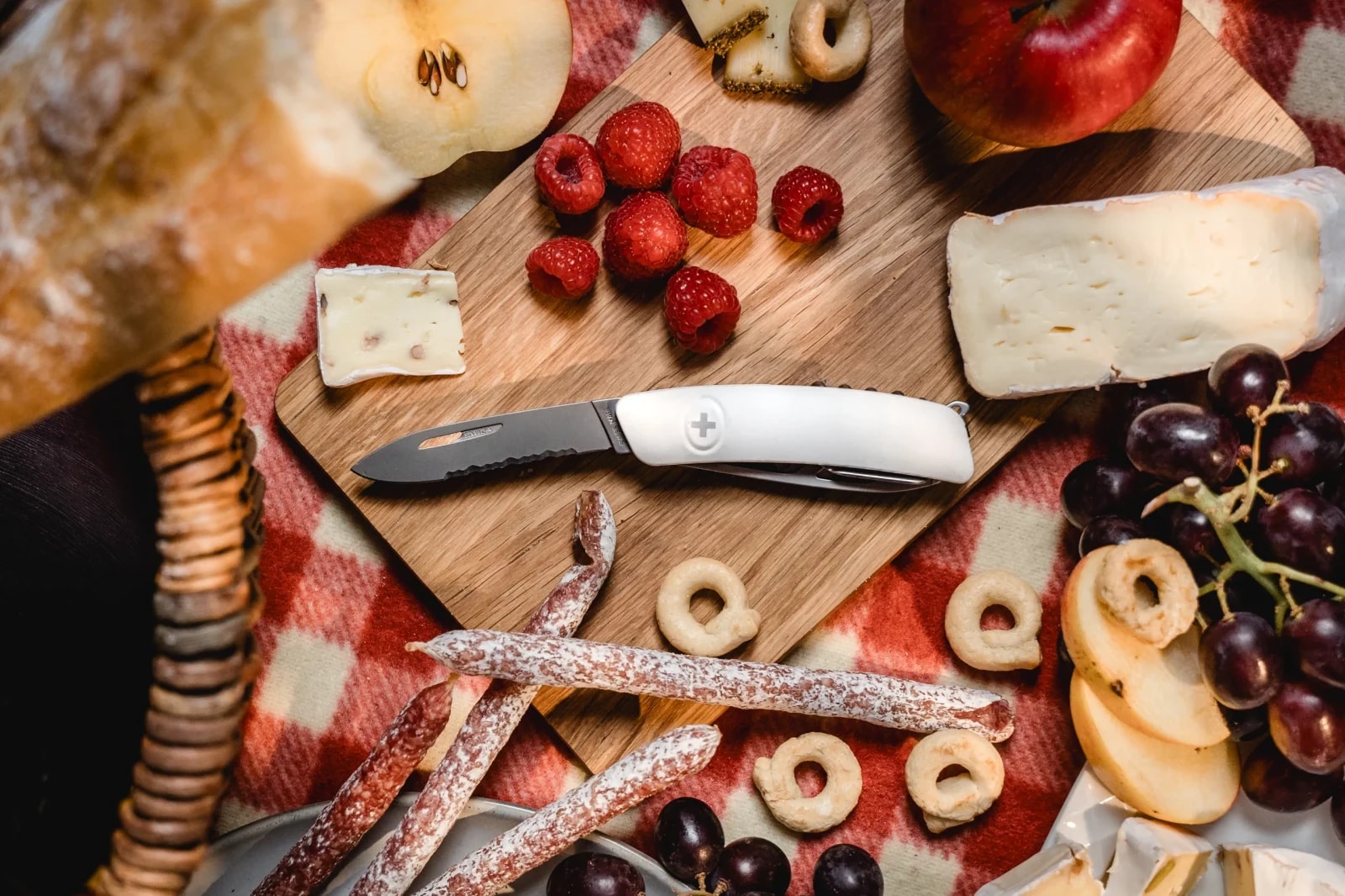 SWIZA Taschenmesser mit weißem Griff auf einem Schneidbrett mit Käse, Beeren, Salami und Brot beim Picknick.