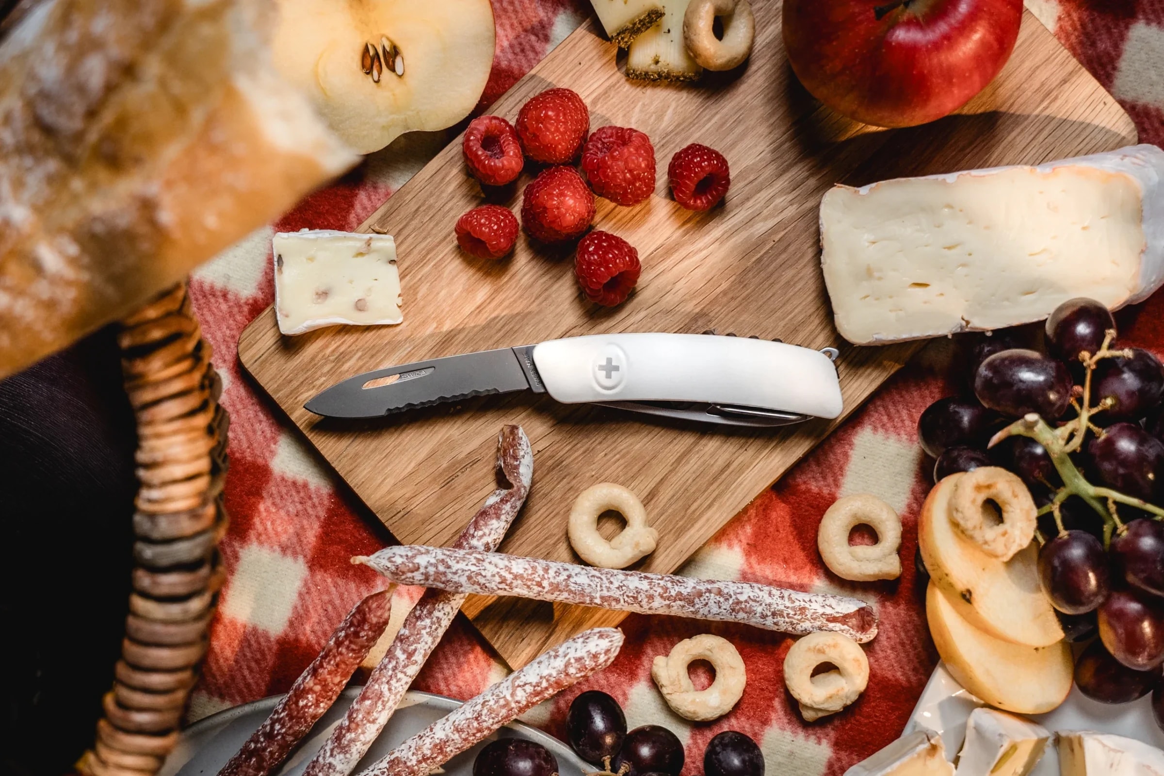 SWIZA Taschenmesser mit weißem Griff auf einem Schneidbrett mit Käse, Beeren, Salami und Brot beim Picknick.