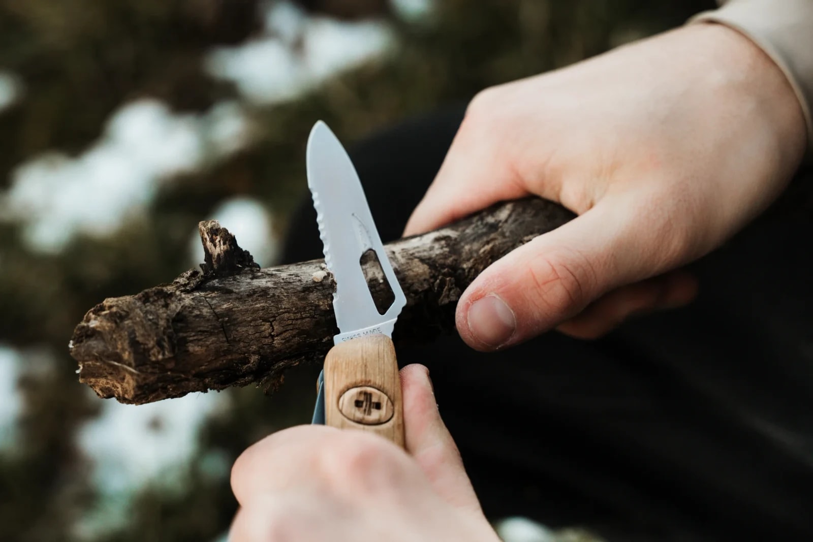 SWIZA Taschenmesser mit Holzgriff beim Schnitzen an einem Ast im winterlichen Wald.