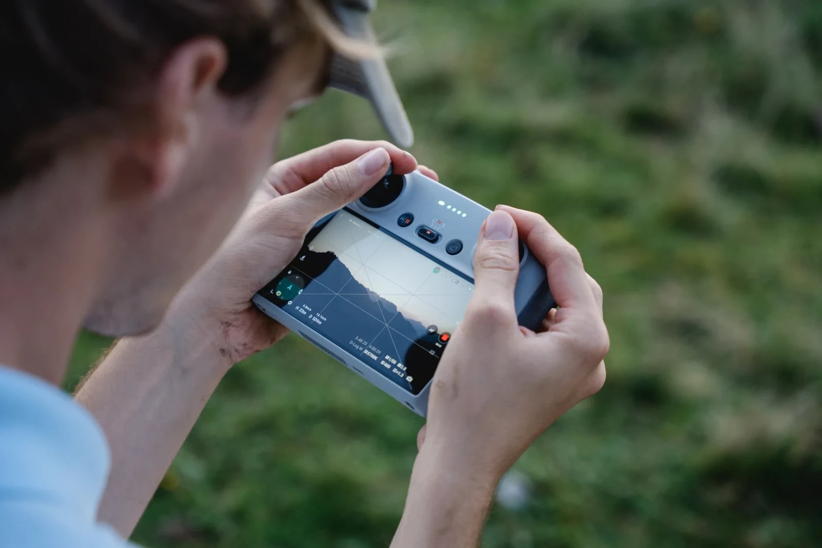 Nahaufnahme: Hände halten eine Drohnen-Fernsteuerung mit Live-Bild einer Bergsilhouette am Display.