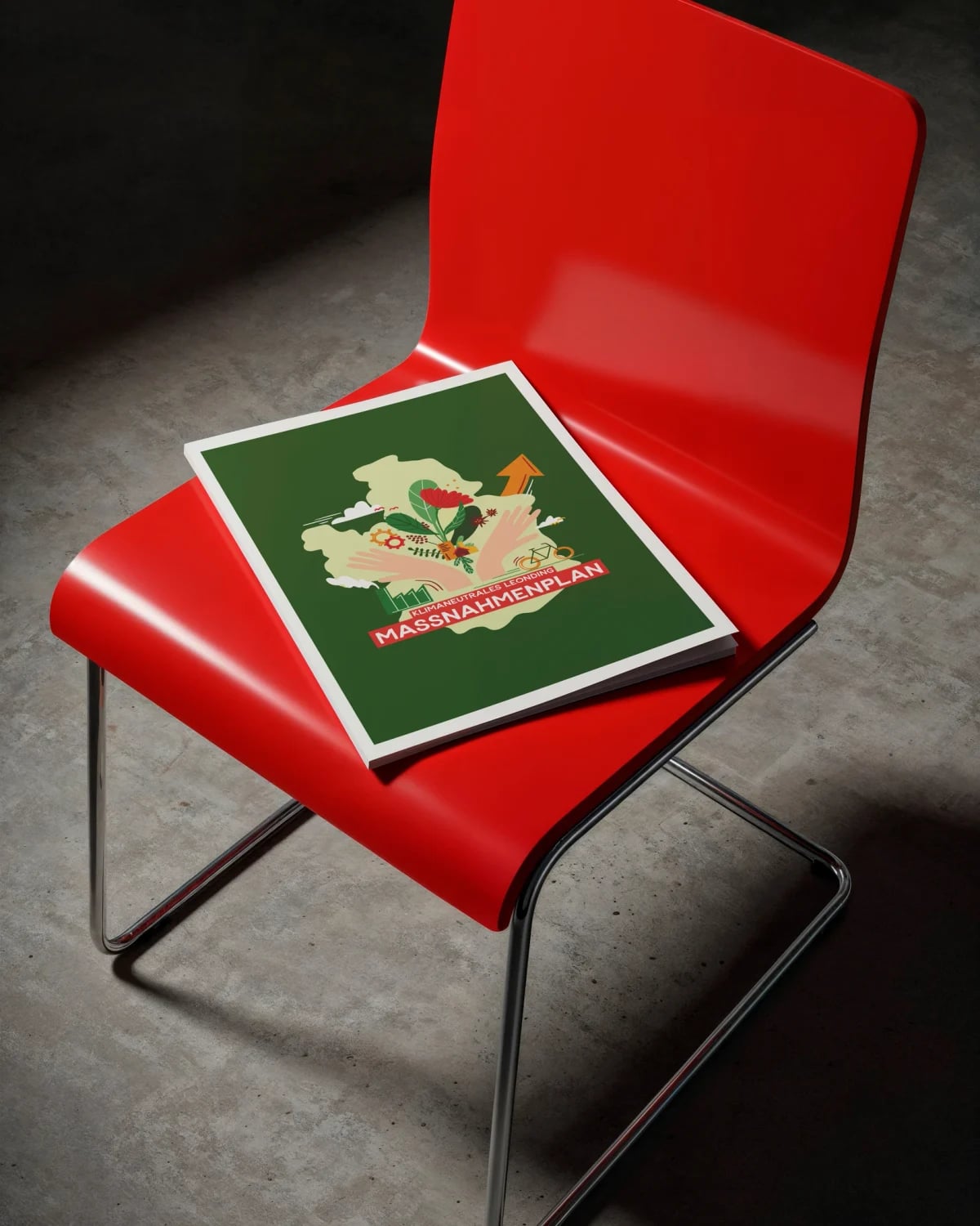 Broschüre „Klimaneutrales Leonding – Maßnahmenplan" mit grünem Cover auf einem roten Designstuhl vor Betonwand.