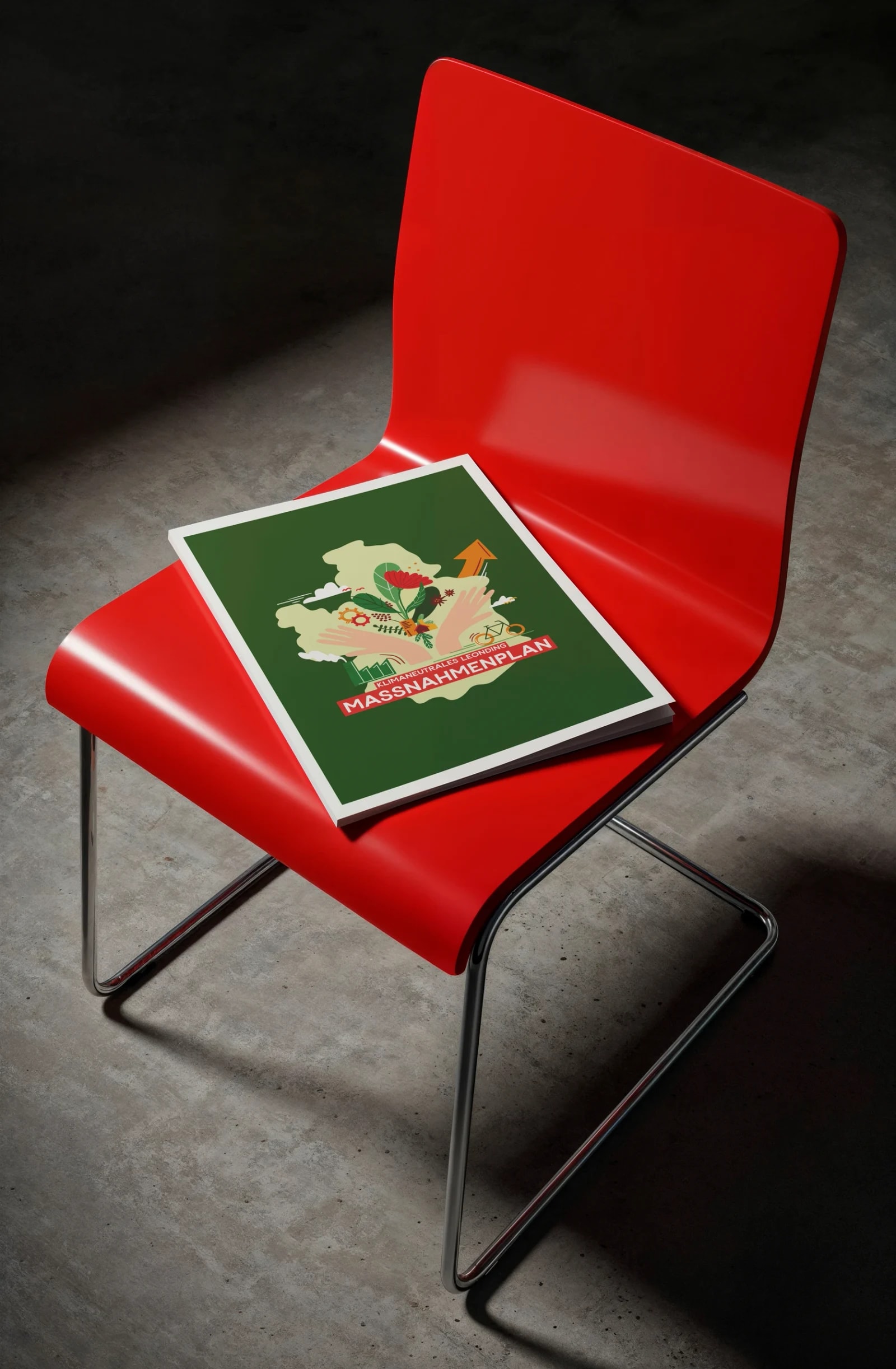 Broschüre „Klimaneutrales Leonding – Maßnahmenplan" mit grünem Cover auf einem roten Designstuhl vor Betonwand.