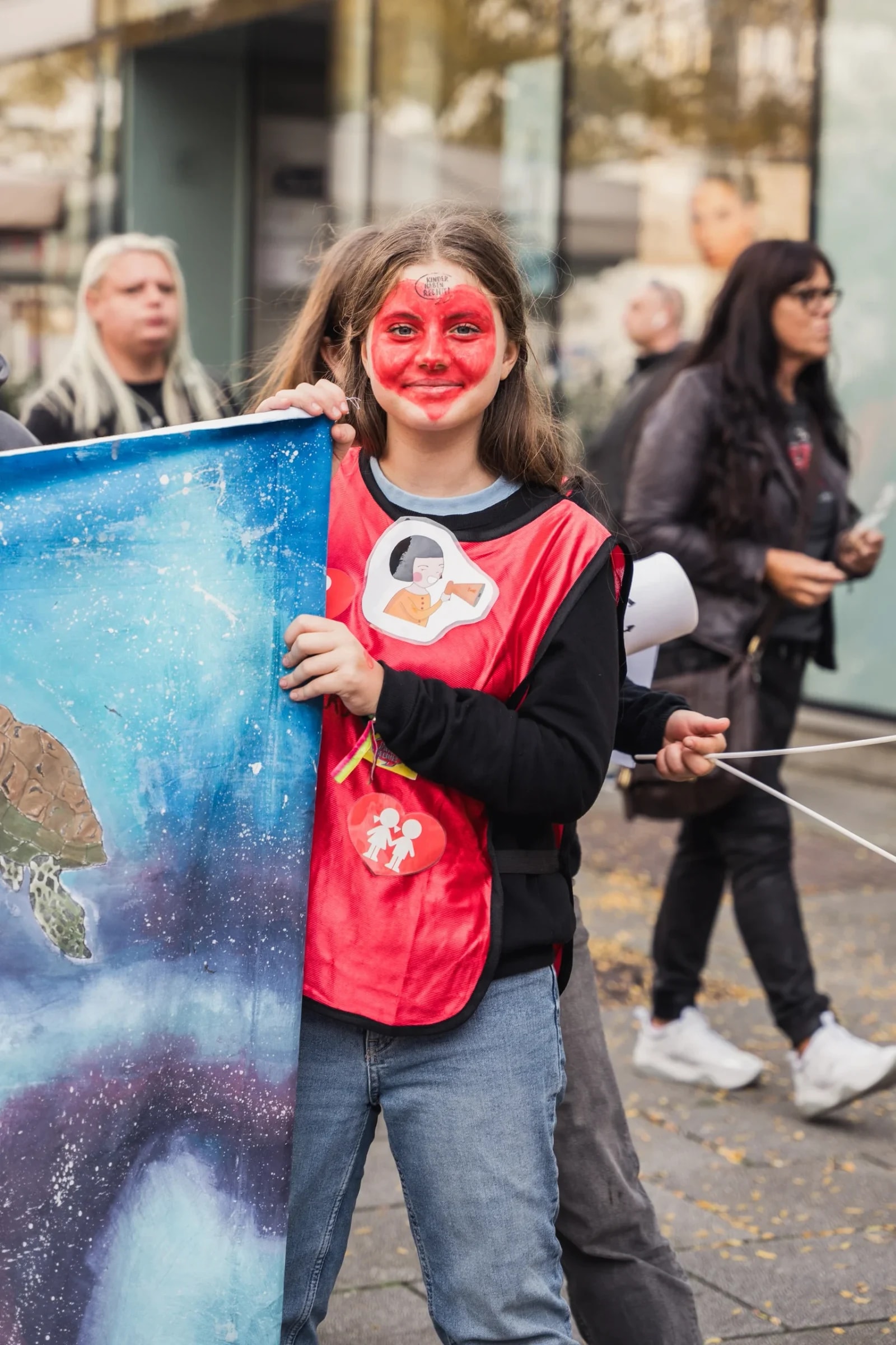 Mädchen mit rot geschminktem Gesicht und Kinderfreunde-Leibchen hält ein selbst gemaltes Klima-Banner.
