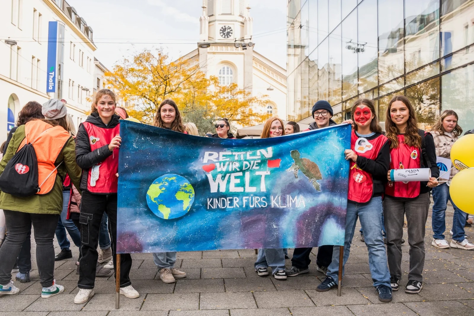 Jugendliche halten ein handgemaltes Banner „Retten wir die Welt – Kinder fürs Klima" bei der Kinderrechte-Demo.