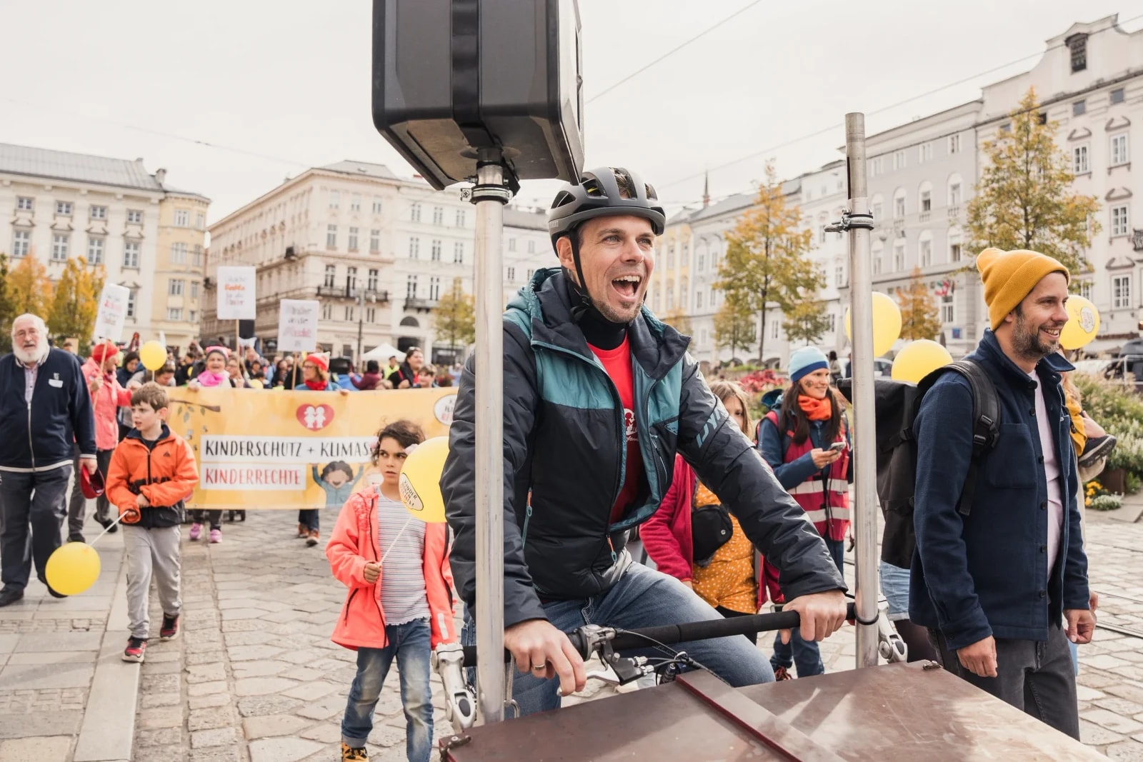 Lachender Mann fährt ein Lastenrad mit Musikanlage an der Spitze des Demozugs, dahinter das Banner „Kinderschutz + Klimaschutz".