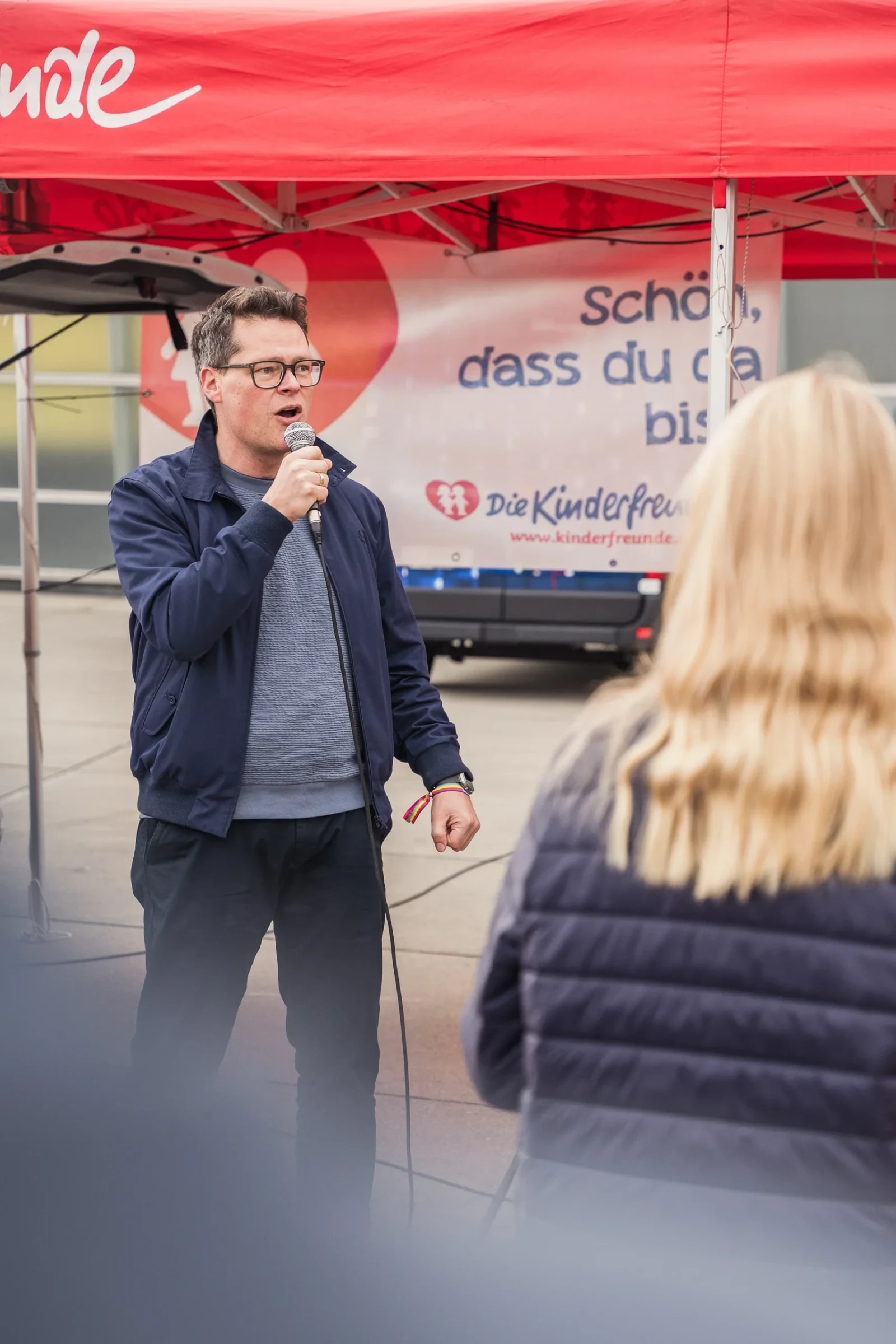 Redner mit Mikrofon unter dem roten Kinderfreunde-Zelt bei der Abschlusskundgebung.