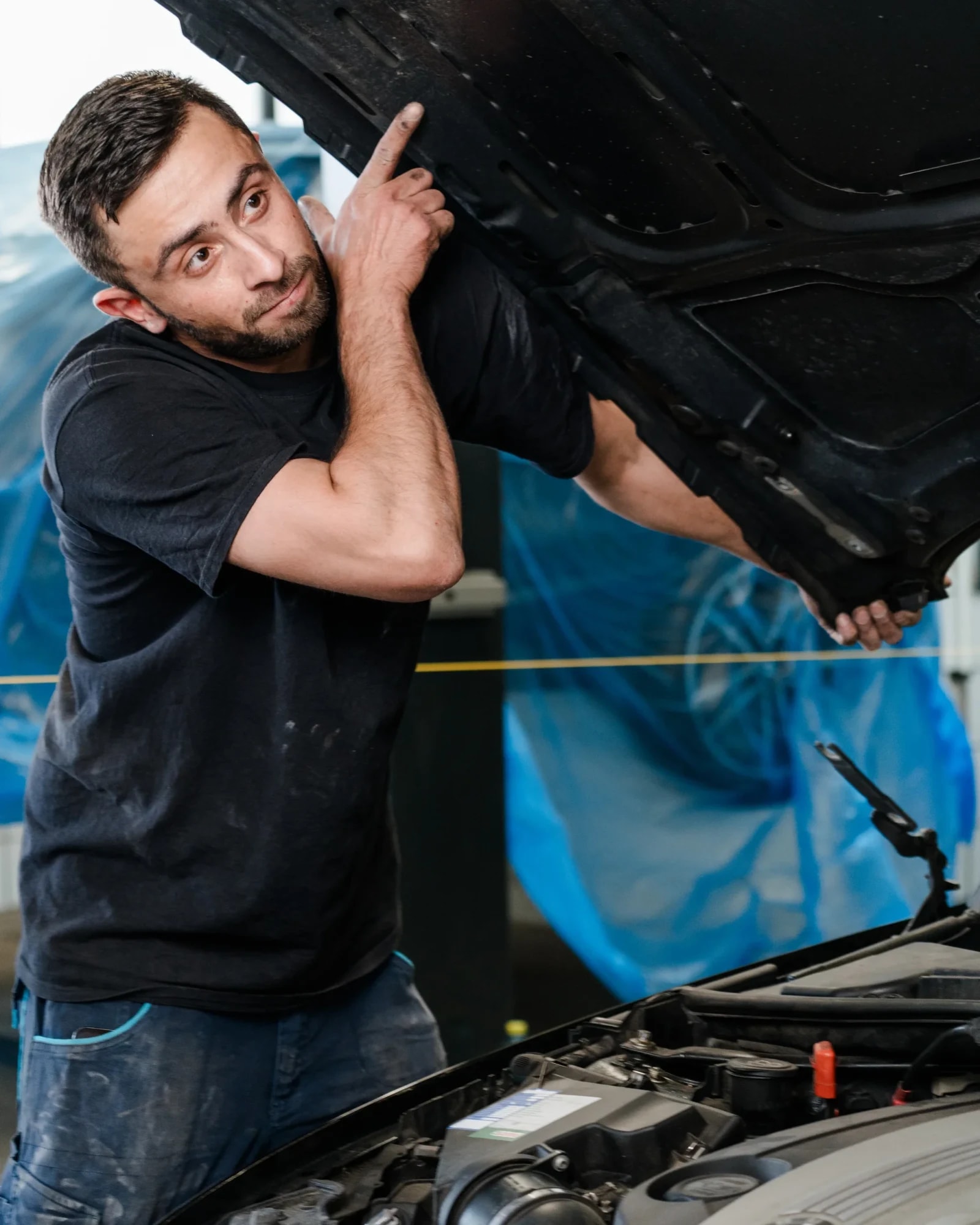 Karosseriebautechniker hebt eine ausgebaute Motorhaube in der Werkstatt an.
