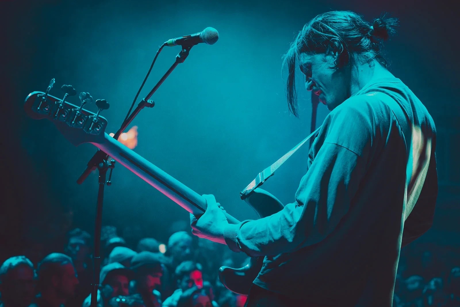 Bassist im türkisen Gegenlicht, davor das Publikum in der ersten Reihe.