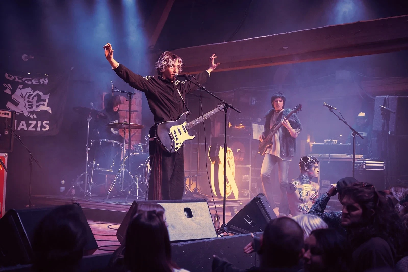 Frontmann mit ausgebreiteten Armen auf der Bühne, dahinter Band und Nebel im violetten Licht.