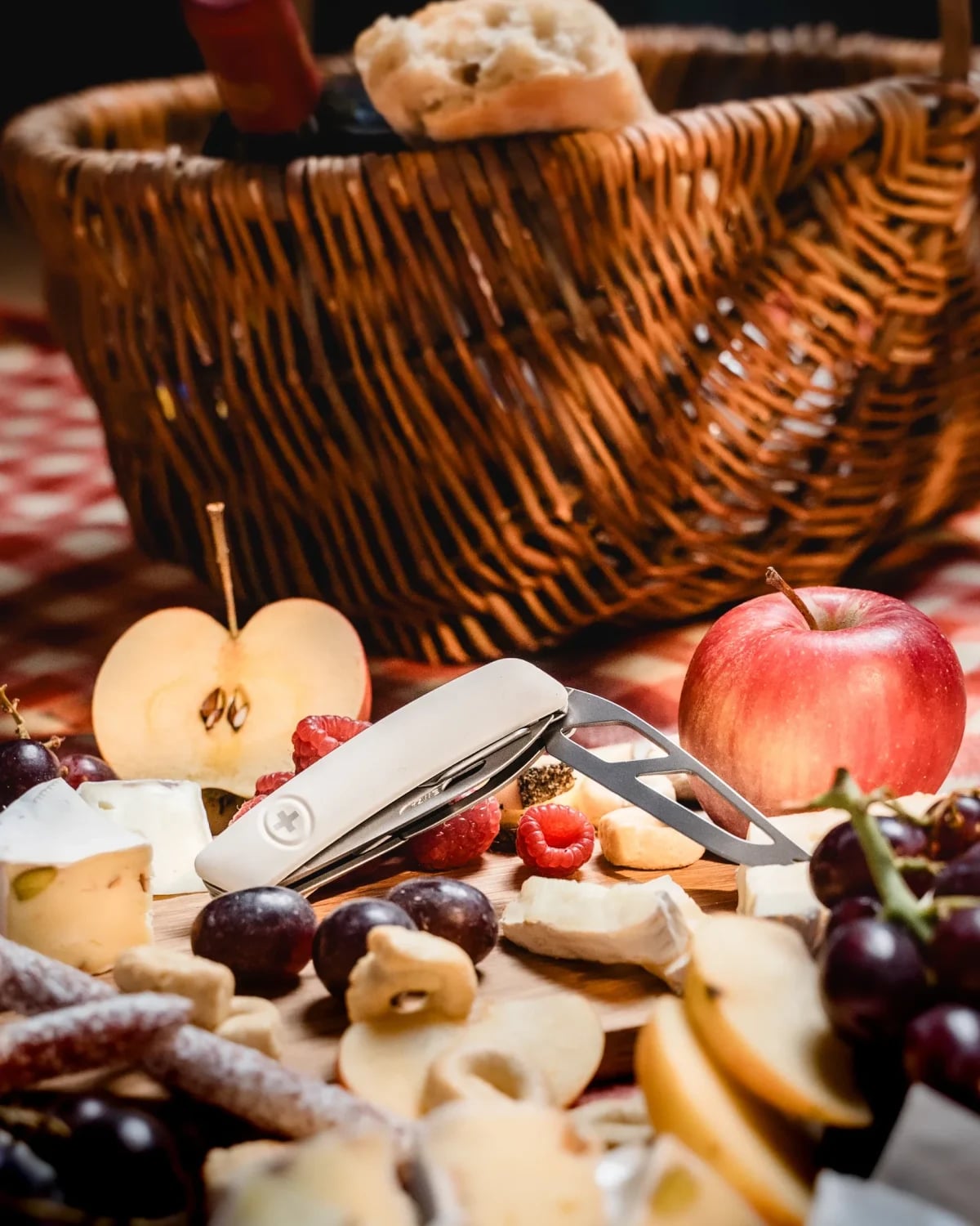 SWIZA Taschenmesser mit ausgeklappter Käsegabel vor einem Weidenkorb mit Wein und Brot.